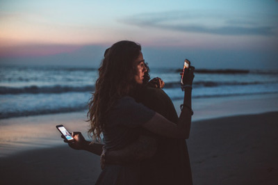 Couple hugging with smartphones in the sunset 